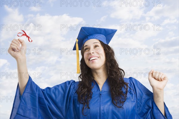 Mixed race woman wearing graduation cap and gown holding diploma