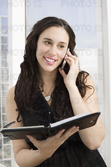 Mixed race businesswoman with notebook talking on cell phone