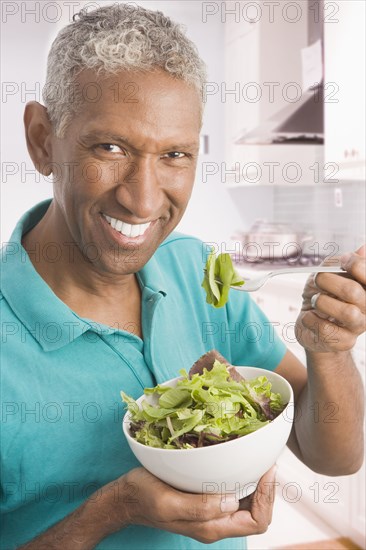 Mixed race man eating salad in kitchen