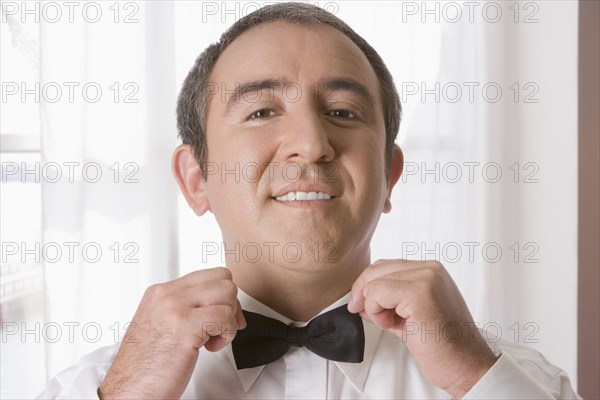 Hispanic man tying bow tie