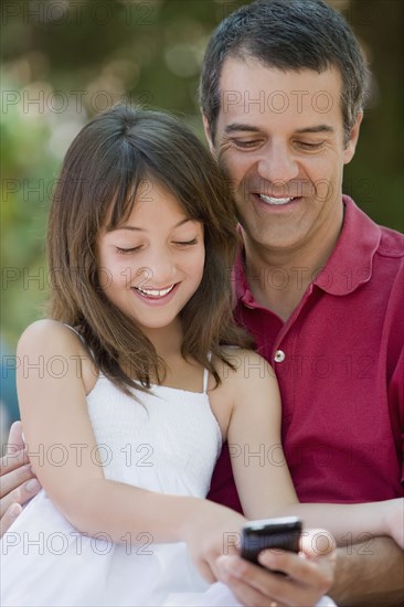 Hispanic father and daughter text messaging on cell phone