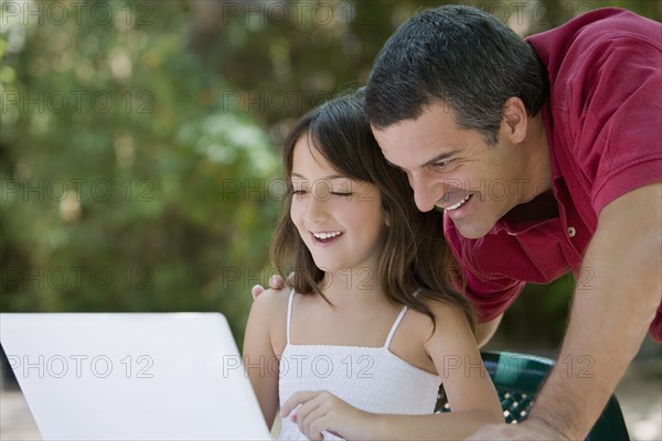 Hispanic father watching daughter use laptop