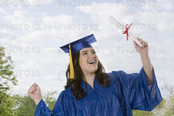 Hispanic teenage girl in graduation cap and gown holding diploma