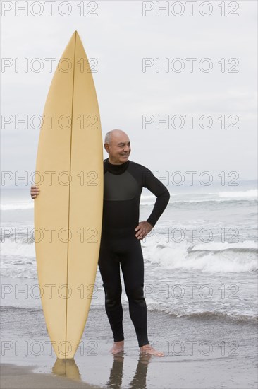 Senior Hispanic man holding surfboard on beach