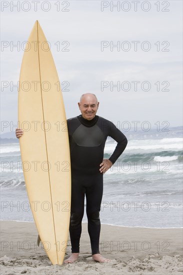 Senior Hispanic man holding surfboard on beach