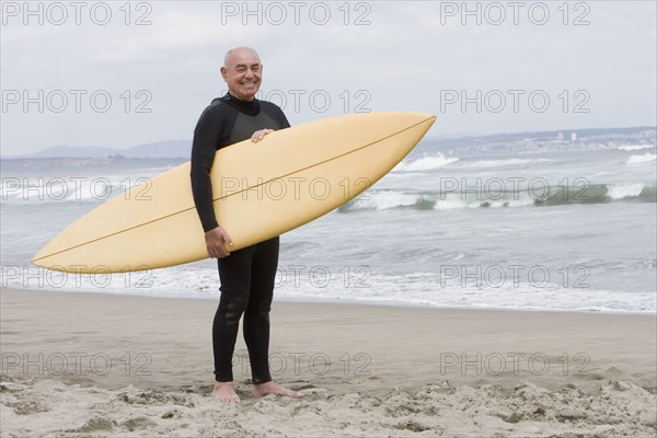 Senior Hispanic man holding surfboard on beach