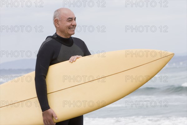 Senior Hispanic man holding surfboard on beach