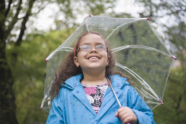 Hispanic girl standing in rain with umbrella