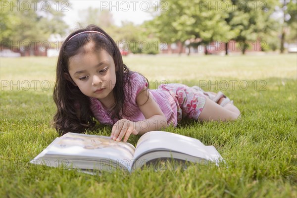 Hispanic girl laying in grass reading book