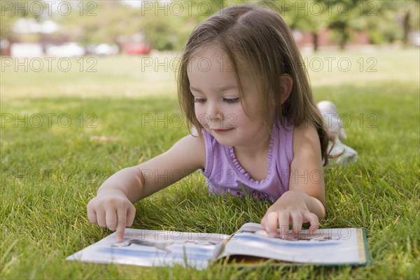 Hispanic girl laying in grass reading book