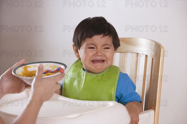 Hispanic mother trying to feed crying baby boy