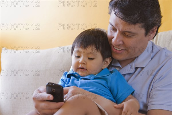 Hispanic father showing cell phone to his son