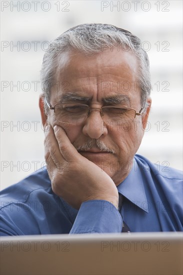 Frowning Hispanic businessman using laptop