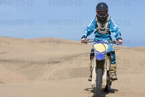 Chilean teenager riding motorcycle on sand dune