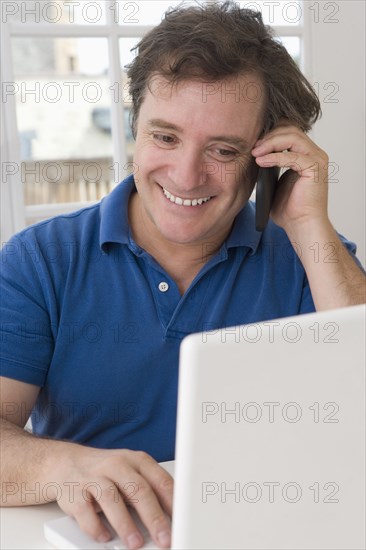 Caucasian man using laptop and talking on cell phone