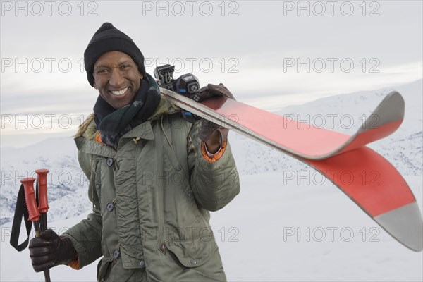 Mixed race man carrying skis on snowy slope
