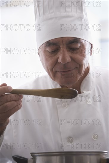 Hispanic chef tasting food in kitchen