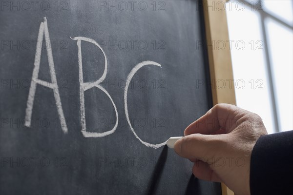 Hispanic teacher writing 'ABC' on chalkboard