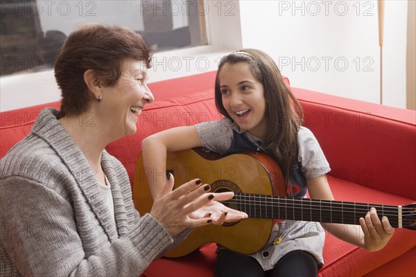 Older Hispanic woman playing music with granddaughter