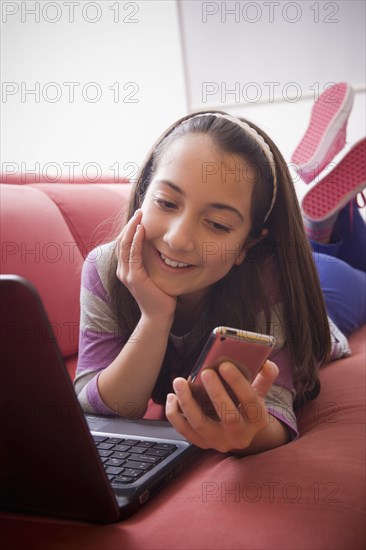 Hispanic girl using laptop and cell phone on sofa