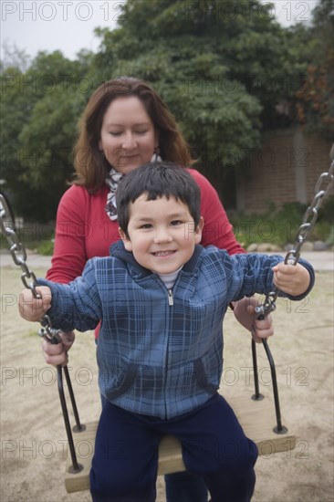 Hispanic mother pushing son on swings