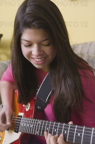 Hispanic girl playing guitar on sofa