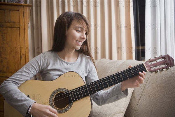 Hispanic girl playing guitar on sofa