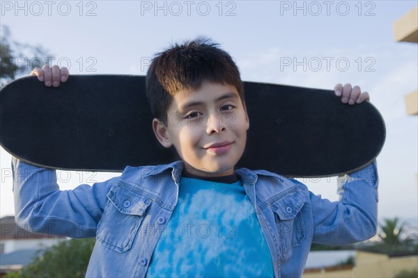 Hispanic boy carrying skateboard