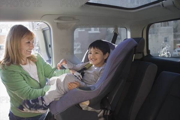 Hispanic woman loading son into car seat