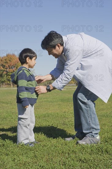 Hispanic father zipping son's sweater in field