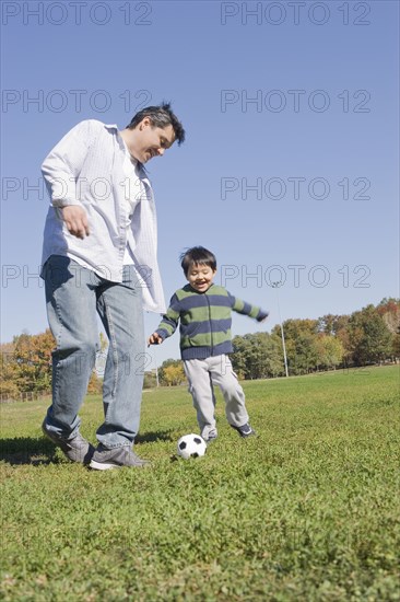 Hispanic father and son playing soccer outdoors