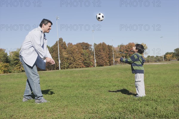 Hispanic father and son playing soccer outdoors