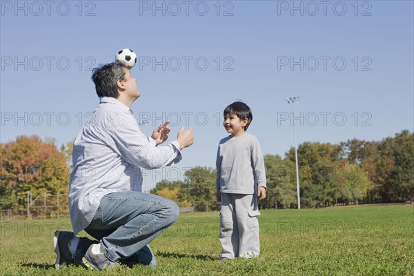 Hispanic father and son playing soccer outdoors