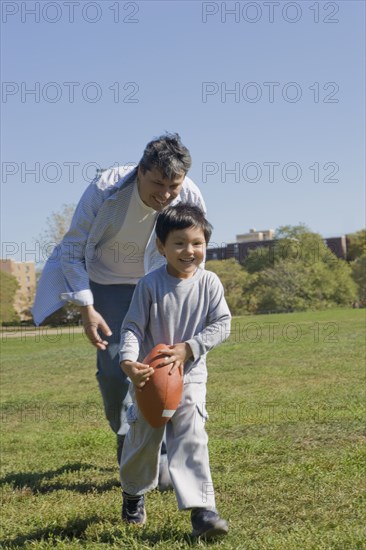 Hispanic father and son playing football outdoors