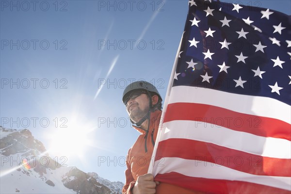 Hispanic hiker planting American flag on snowy mountain