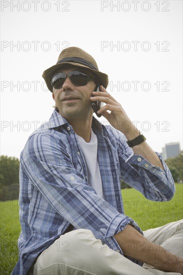 Hispanic man talking on cell phone in grass at park