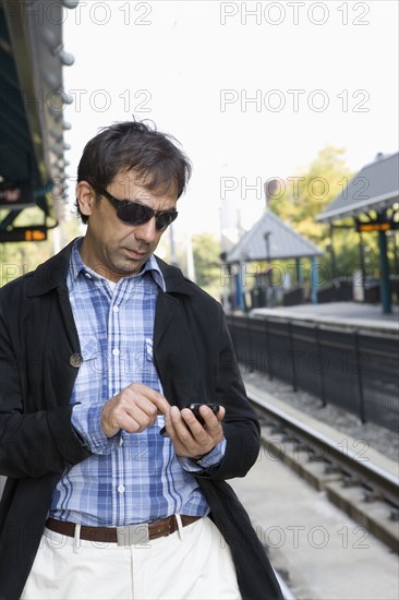 Hispanic man text messaging on train station platform