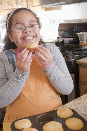 Portrait of smiling Hispanic girl eating muffin in kitchen