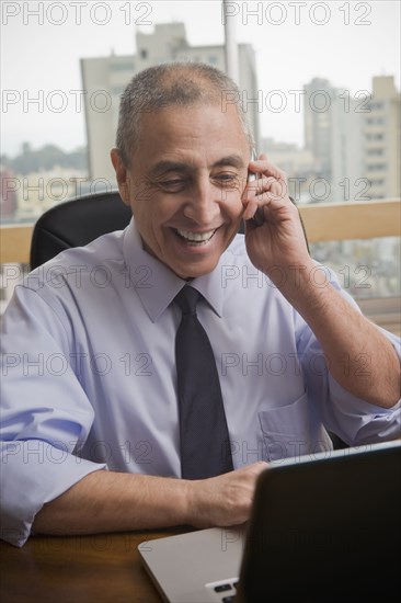 Hispanic businessman using cell phone and laptop in office