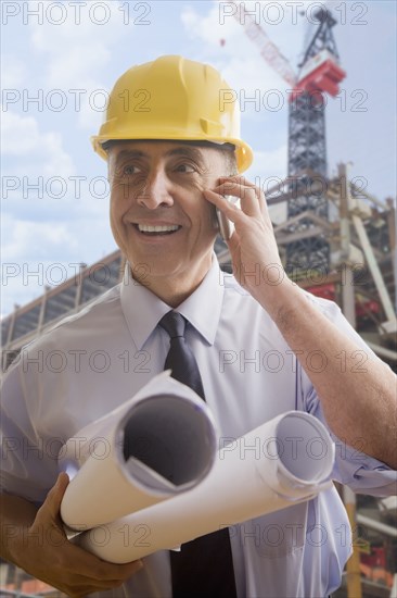 Hispanic architect talking on cell phone at construction site