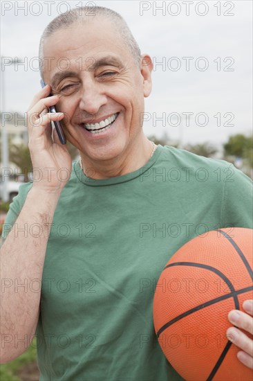 Hispanic senior man with basketball talking on cell phone