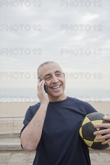 Hispanic senior man with soccer ball talking on cell phone