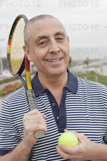 Hispanic senior man carrying tennis racket and ball