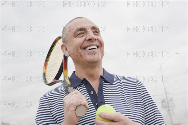 Hispanic senior man carrying tennis racket and ball