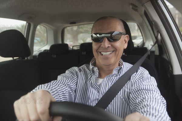 Hispanic senior man in sunglasses driving car