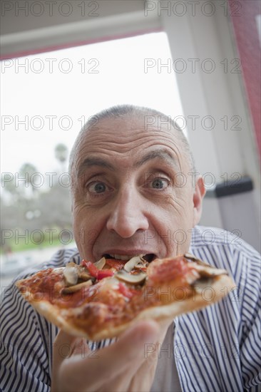 Hispanic senior man eating slice of pizza