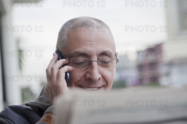 Hispanic senior man talking on cell phone and reading newspaper