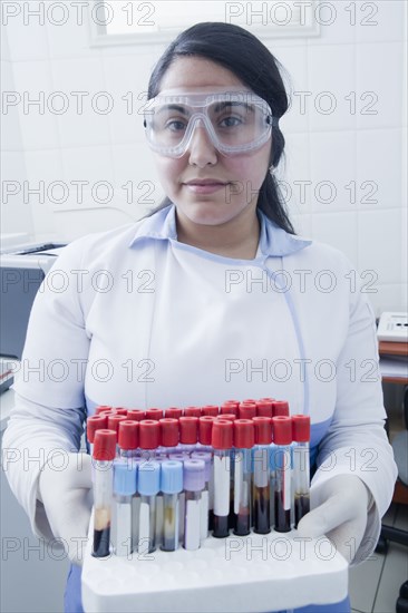 Hispanic scientist holding blood samples in test tube rack in laboratory