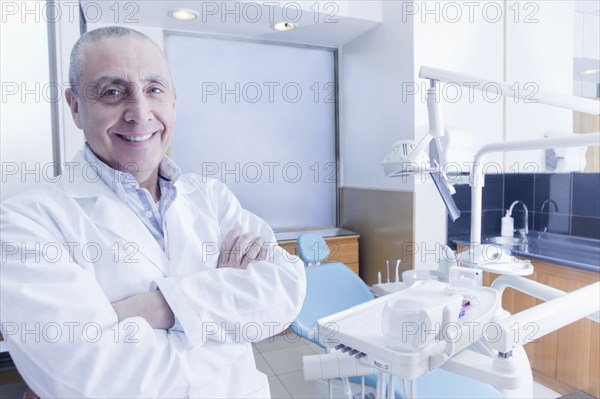 Hispanic dentist smiling near chair in office