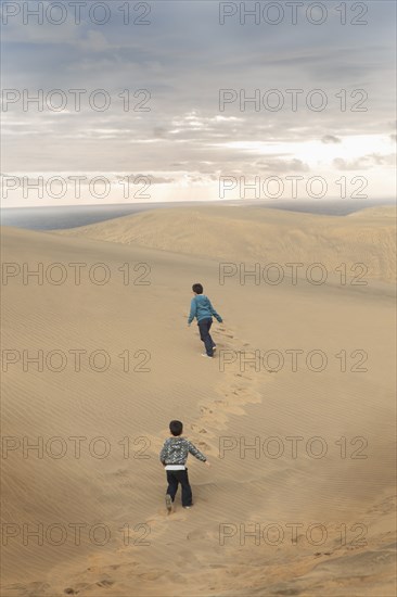 Hispanic brothers running on sand dunes